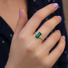 a woman's hand wearing a ring with an emerald stone and diamond accented band