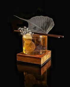 a glass filled with liquid next to a leaf on top of a wooden block,