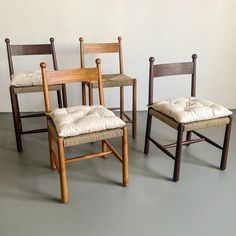 three wooden chairs sitting next to each other on a gray floor in front of a white wall