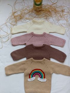 four knitted sweaters with rainbow and clouds on them, all in different colors