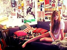 a woman sitting on top of a couch in a room with posters all over the wall