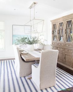 a dining room table and chairs in front of a wooden hutch with striped rug