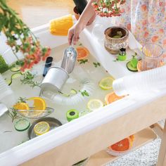 a person pouring water into a sink filled with lemons, limes and orange slices