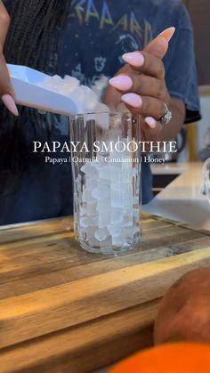 a woman is pouring water into a glass with ice cubes on the side and an orange behind her