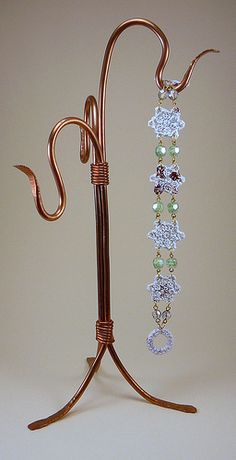 a pair of earrings is hanging from a stand on a white surface with a light brown background