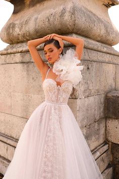 a woman in a white wedding dress leaning against a stone wall with her hands on her head