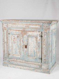 an old blue cabinet with peeling paint on the doors and drawers is against a white background