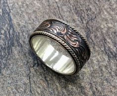 a silver ring with an intricate design on it sitting on a stone surface in front of a rock