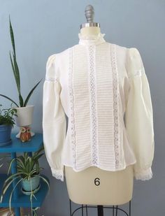 Vintage 80's Victorian blouse. Off white silk with high lace ruffle collar, eyelet lace, horizontal pleats and button lace cuffs. Button down back with billowy long sleeves with puffed shoulders. Sightly sheer overall. Straight hem. Gorgeous top would be great for a formal event.  Fits up to a size large. Please double-check the measurements below: MEASUREMENTS--Taken with garment laying flat, in inches, doubled: Bust: 40"  Waist: 38"  Shoulder: 14" Length: 23" {top neck to bottom hem} Neck: 14" Sleeve length: 24.5" Label/ Era: Royal Silk | 1980 Stated Size: 8 Fabric: Silk, acrylic buttons Condition: Excellent condition. Freshly laundered. No known issues.  ★ Shop entire shop here: https://www.etsy.com/shop/retrosuzysvintage Instagram | retrosuzysvintage Facebook | retrosuzysvintage Pinter Victorian Blouse, Lace Cuffs, Ruffle Collar, Eyelet Lace, Lace Ruffle, White Silk, Lace Blouse, Silk Blouse, Formal Event