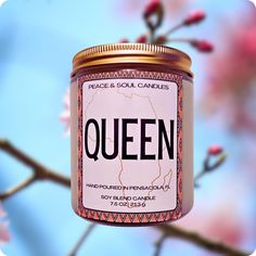 a candle with the word queen on it hanging from a tree branch in front of some pink flowers