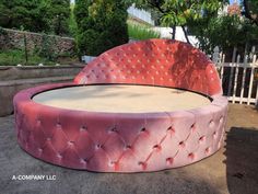 a pink round bed sitting on top of a cement ground next to a tree and fence