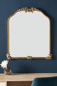 a gold framed mirror sitting on top of a wooden table next to a blue chair