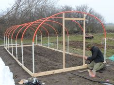 a man kneeling down in front of a garden plot with an orange arch over it