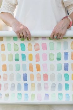 a woman is holding a watercolor painting on a white surface with her hands in the frame