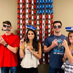 group of people with fake mustaches and hats posing in front of an american flag backdrop