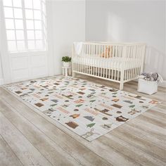 a baby's room with a white crib and wooden flooring that has an animal themed rug on it