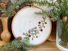 some pine cones and needles are sitting on a table next to a cross - stitch hoop