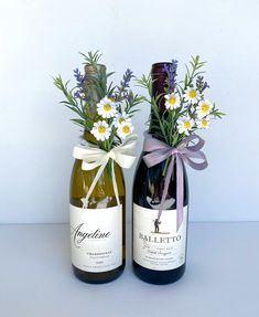 two wine bottles with flowers in them sitting next to each other