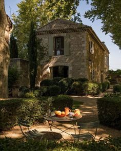 an outdoor table with oranges on it in front of a stone house surrounded by trees