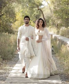 a man and woman in white outfits walking down a path with trees behind their backs