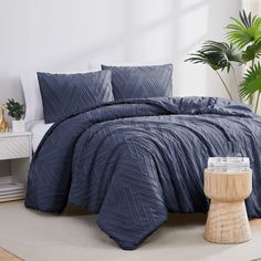 a bed with blue comforter and pillows in a room next to a potted plant