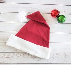 a red and white santa claus hat next to two christmas ornaments on a wooden table