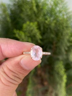 a person holding an engagement ring with a pink stone in their left hand and diamond band around it