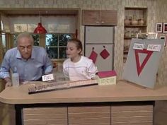 an older man and young woman sitting at a kitchen counter with boxes on it,