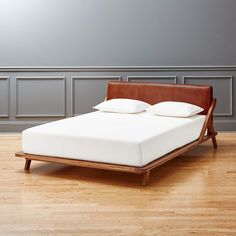 a bed sitting on top of a hard wood floor next to a white wall and wooden headboard