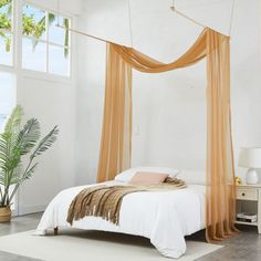 a bedroom with a white bed and orange drapes hanging from the ceiling over it