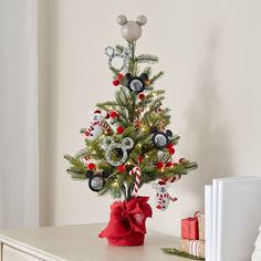 a small christmas tree with mickey mouse ornaments on it's top and a red bow