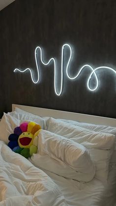 a teddy bear sitting on top of a bed under a neon sign that reads hello