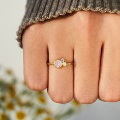 a person's hand with a ring on it and flowers in the background,