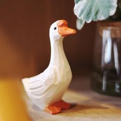 a paper mache duck next to a plant in a vase on a wooden table