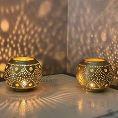 two decorative candle holders sitting on top of a white table next to a wall covered in lights