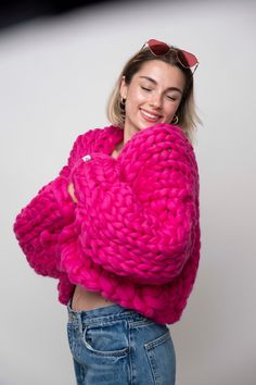 a woman wearing sunglasses and a pink sweater poses for the camera with her arms crossed