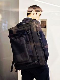 a young man carrying a black backpack while standing in front of a wall with his back to the camera