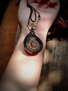 a woman's hand holding a brown and black necklace with a pendant on it