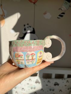 a hand holding a small cup with designs on the outside and inside, in front of a wallpapered background