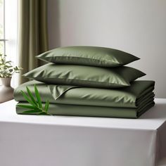 a stack of green pillows sitting on top of a white table next to a potted plant