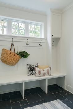 a white bench with some pillows and a basket hanging on it's back wall