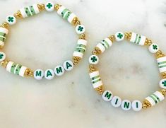 two bracelets with green and white beads are sitting on a marble surface, one has the word mama written in gold