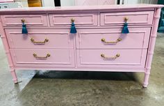 a pink dresser with gold handles and blue tassels on the drawers is shown