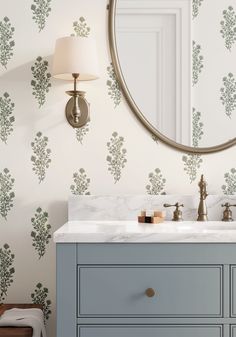 a bathroom vanity with a round mirror above it and wallpaper on the walls behind it