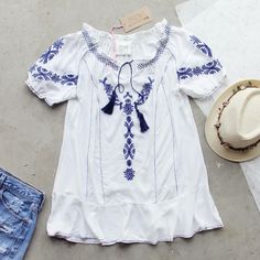 Gorgeous embroidered details adorn this tunic. Designed with a soft white base, navy embroidered details throughout, a tassel tie neck, short sleeves, and a breezy tunic fit. Color: White & navy 65% cotton & 34% rayon Imported Hand wash cold split Small/Medium Medium/Large Bust 38 40 Waist 37 39 Hips 39 41 Length 30 30 Bust, waist, and hip measurements are a total circumference. Length is measured from the top of the top to the hem. Measurements are an estimate. Casual Tunic Top With Tassels, Summer Blouse With Floral Embroidery And Short Sleeves, Blue Tassel Blouse For Summer, Bohemian Peasant Top With Embroidered Hem For Summer, Bohemian Summer Peasant Top With Embroidered Hem, Casual Floral Embroidery Peasant Tunic Top, Summer Peasant Blouse With Tassels, Spring Bohemian Embroidered Short Sleeve Top, Peasant Style Summer Blouse With Tassels