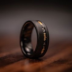 a black ring with gold inlays sitting on top of a wooden table