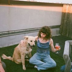 a woman sitting on the grass with her dog and holding a wine glass in front of her