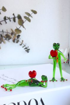 two figurines sitting on top of a white box next to each other, one holding a heart