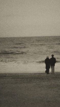 two people standing on the beach looking out at the ocean