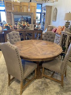 a round wooden table surrounded by chairs and other furniture in a room with lots of windows